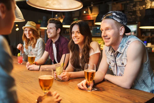 Счастливые друзья с напитками, беседующие в баре или пабе — стоковое фото