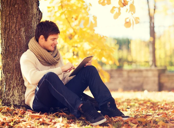 Glimlachend jongeman met de tablet pc in de herfst park — Stockfoto