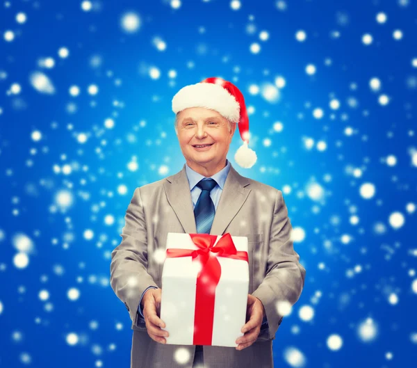 Uomo sorridente in abito e cappello da Babbo Natale con regalo — Foto Stock