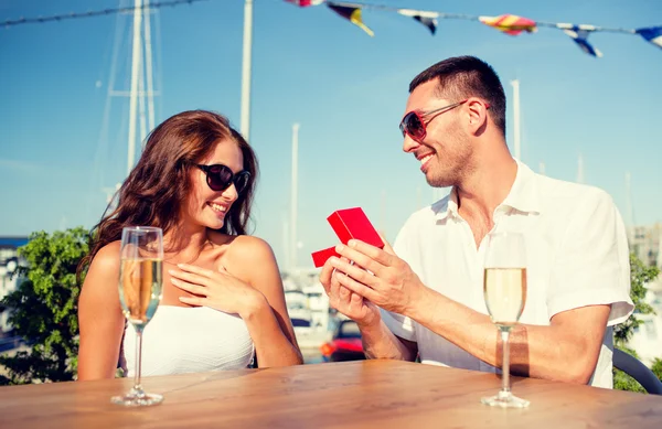 Pareja sonriente con champán y regalo en la cafetería —  Fotos de Stock