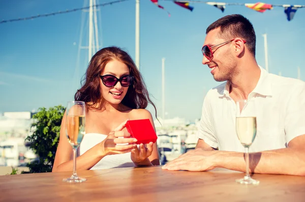 Smiling couple with champagne and gift at cafe — Stock Photo, Image