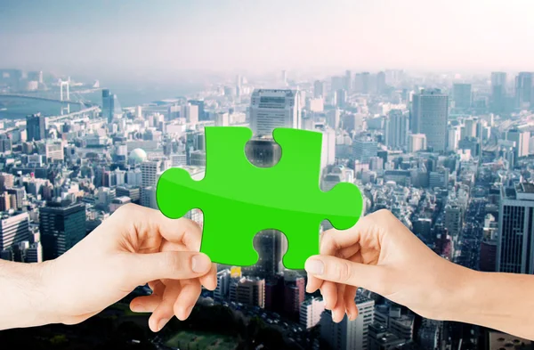Hands with green puzzle over city background — Stockfoto