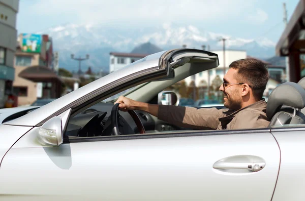 Happy man driving cabriolet car over city in japan — Stock Photo, Image