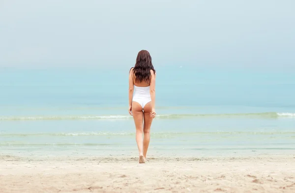Νεαρή γυναίκα με μαγιό περπάτημα στην παραλία — Φωτογραφία Αρχείου
