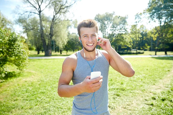 Счастливый человек с наушниками и смартфоном в парке — стоковое фото