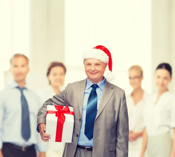 Hombre sonriente en traje y sombrero de ayudante de santa con regalo —  Fotos de Stock