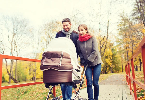 Pareja sonriente con cochecito de bebé en el parque de otoño — Foto de Stock