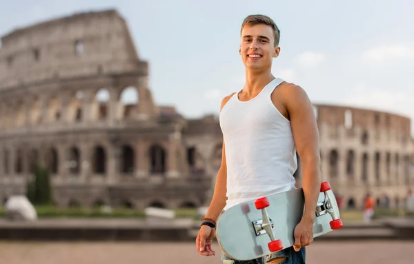 Улыбающийся подросток со скейтбордом над Колизеем — стоковое фото