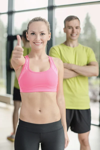 Sonriente hombre y mujer mostrando pulgares hacia arriba en el gimnasio — Foto de Stock