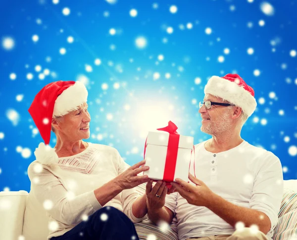 Felice coppia di anziani in cappelli di Babbo Natale con scatola regalo — Foto Stock