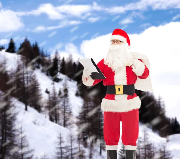 Homem em traje de santa claus com bloco de notas e saco — Fotografia de Stock