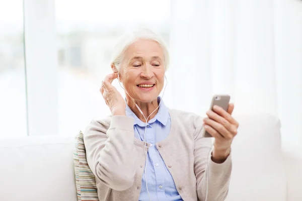 Mulher idosa com smartphone e fones de ouvido em casa — Fotografia de Stock