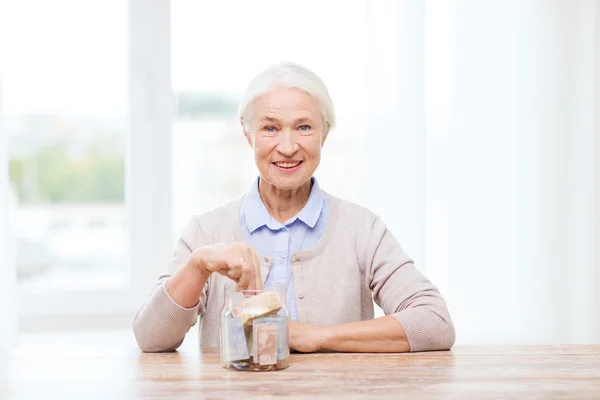 Donna anziana mettendo soldi in vaso di vetro a casa — Foto Stock