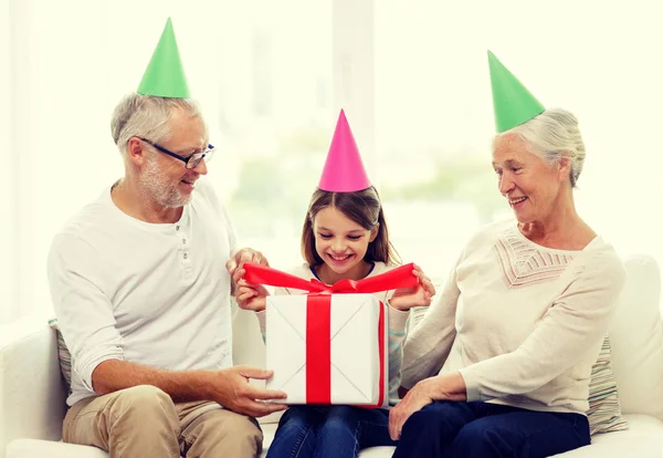 Familia sonriente en sombreros de fiesta con caja de regalo en casa —  Fotos de Stock