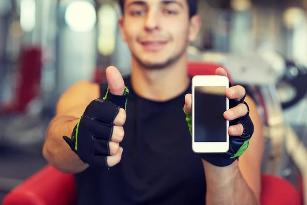 Joven con smartphone mostrando pulgares hacia arriba en el gimnasio — Foto de Stock