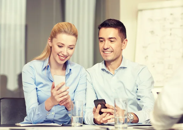Uomini d'affari sorridenti con smartphone in ufficio — Foto Stock
