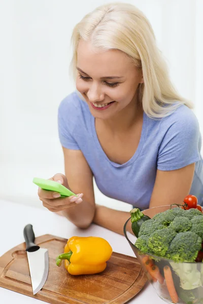 Mujer sonriente con smartphone cocinar verduras — Foto de Stock