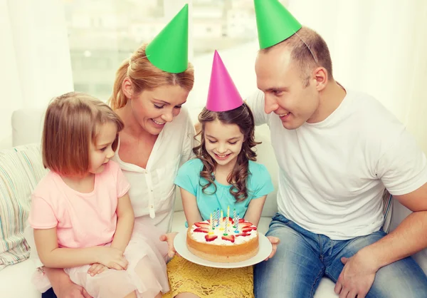 Lachende gezin met twee kinderen in hoeden met cake — Stockfoto