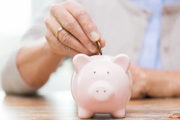 Senior woman hand putting money to piggy bank — Stock Photo, Image