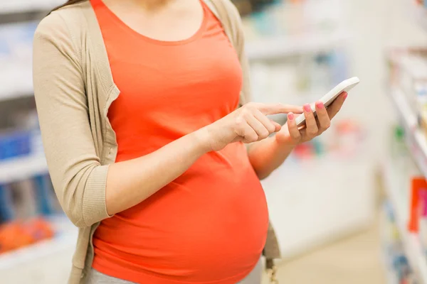 Těhotná žena s smartphone v lékárně — Stock fotografie