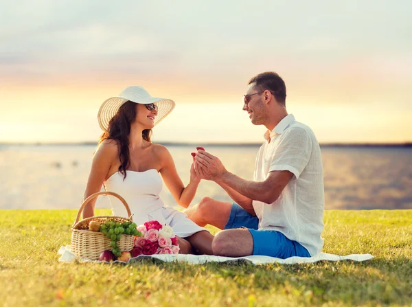 Sonriente pareja con pequeña caja de regalo roja en el picnic — Foto de Stock