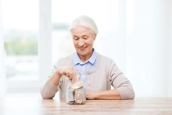 Mulher sênior colocando dinheiro em jar — Fotografia de Stock