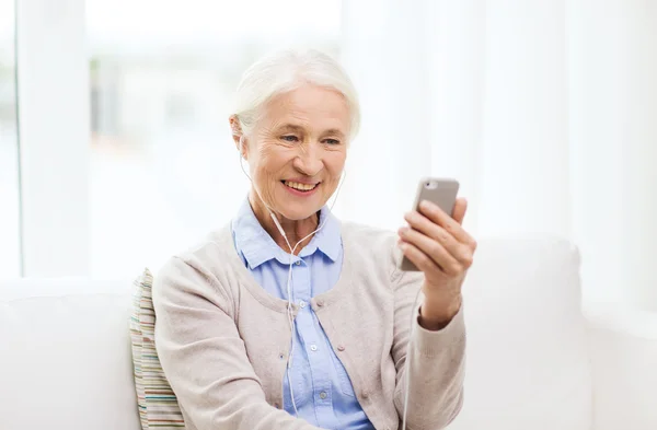 Äldre kvinna med smartphone och hörlurar hemma — Stockfoto