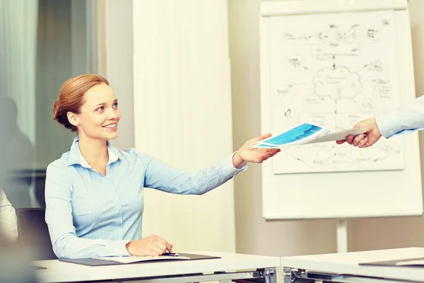 Business woman taking papers from someone in office — стоковое фото