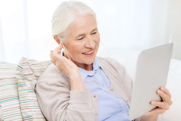 Donna anziana con tablet pc e auricolari a casa — Foto Stock