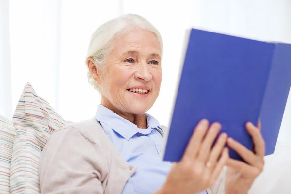 Счастливая улыбающаяся пожилая женщина читает книгу дома — стоковое фото
