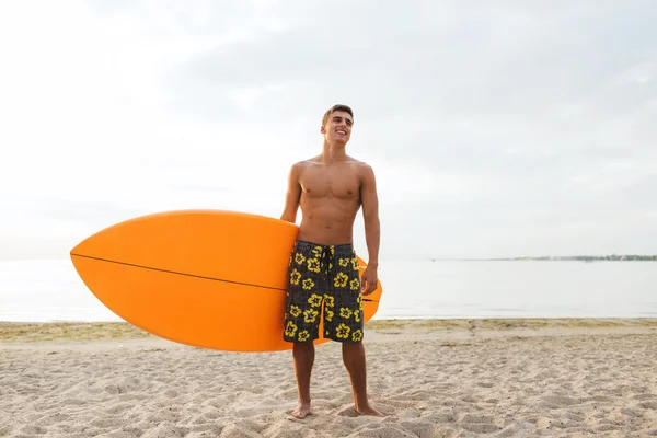 Усміхнений молодий чоловік з дошкою для серфінгу на пляжі — стокове фото