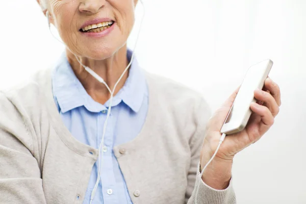 Счастливая пожилая женщина со смартфоном и наушниками — стоковое фото
