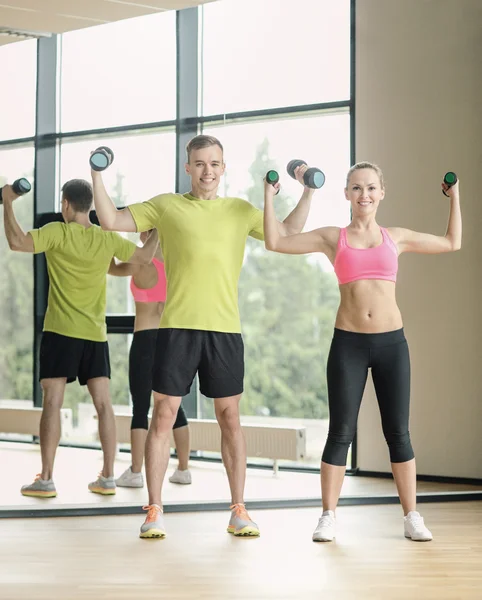 Sonriente hombre y mujer con mancuernas en el gimnasio — Foto de Stock