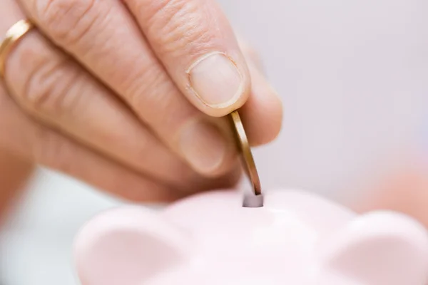 Senior woman hand putting money to piggy bank — Stock Photo, Image