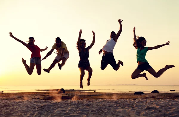 Smiling friends dancing and jumping on beach — Stock Photo, Image