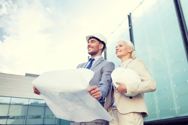 Smiling businessmen with blueprint and helmets — Stock Photo, Image