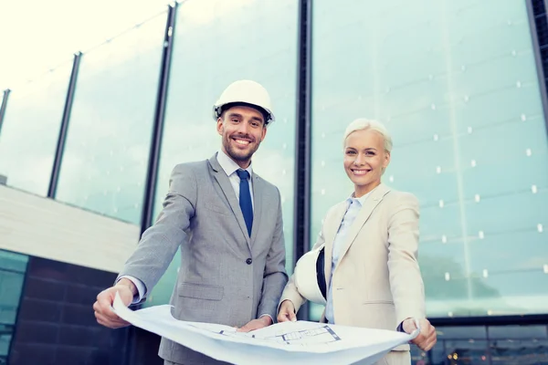 Glimlachende zakenmensen met blauwdruk en helmen — Stockfoto