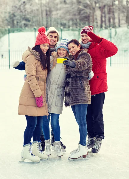 Amigos felices con smartphone en pista de patinaje sobre hielo — Foto de Stock