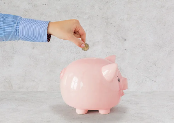 Fechar a mão colocando moeda para o banco porquinho — Fotografia de Stock