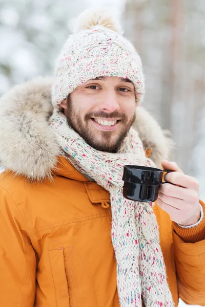 Улыбающийся молодой человек с чашей в зимнем лесу — стоковое фото