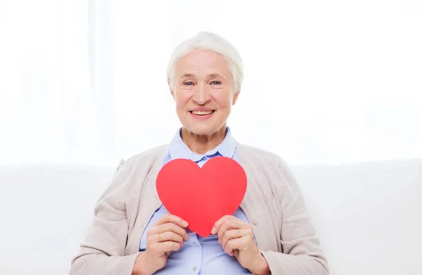 Heureuse femme âgée souriante avec le coeur rouge à la maison — Photo