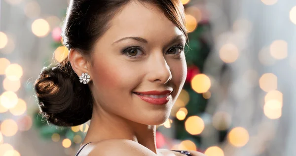Woman with diamond earring over christmas lights — Stockfoto