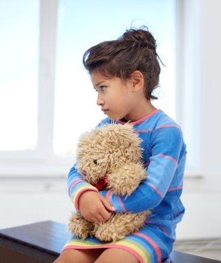 sad little girl with teddy bear toy at home clipart