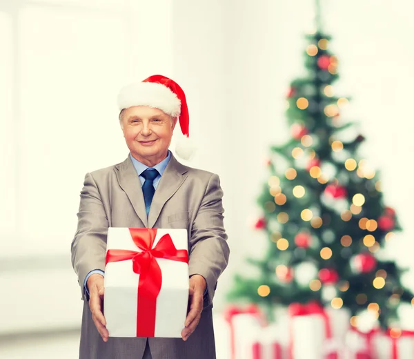 Hombre sonriente en traje y sombrero de ayudante de santa con regalo —  Fotos de Stock