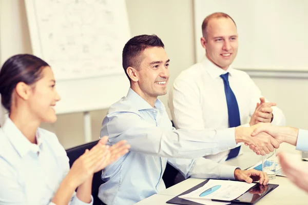 Smiling business team shaking hands in office — Stock Photo, Image