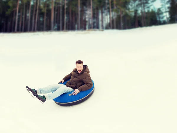 Heureux jeune homme glissant vers le bas sur la neige tube — Photo