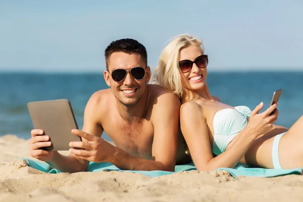 Gelukkige paar met de tablet pc om te zonnebaden op het strand — Stockfoto