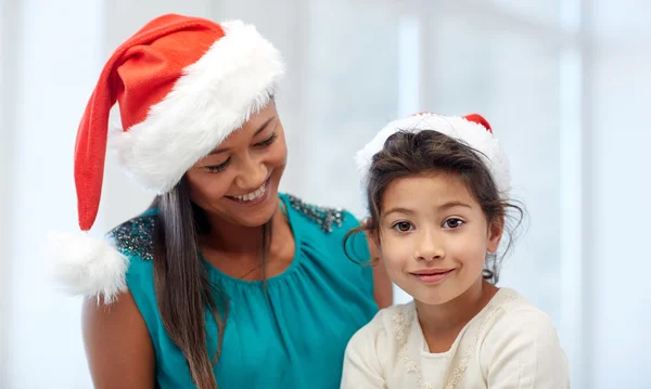 Felice madre e bambina in cappelli di Babbo Natale a casa — Foto Stock