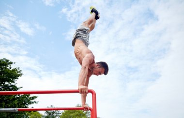 young man exercising on parallel bars outdoors clipart