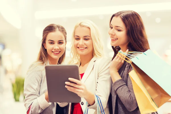 Mulheres jovens felizes com tablet pc e sacos de compras — Fotografia de Stock